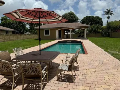 a table and chairs with an umbrella next to a pool at Miami Mansion for Groups Sleeps 12 in Kendale Lakes