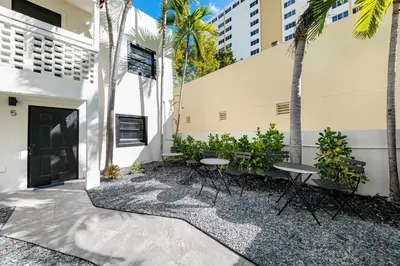 a patio with tables and palm trees in front of a building at Art Deco Gem Steps to Beach in Miami Beach