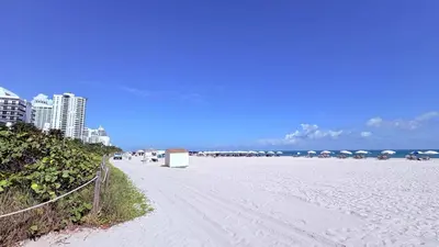 a white sandy beach with umbrellas and the ocean at Art Deco Gem Steps to Beach in Miami Beach
