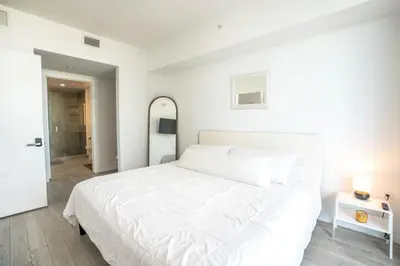 a white bedroom with a white bed and a mirror at Downtown Miami 2BR Retreat - Walk to Bayside & Port - Sleeps 6 in Miami