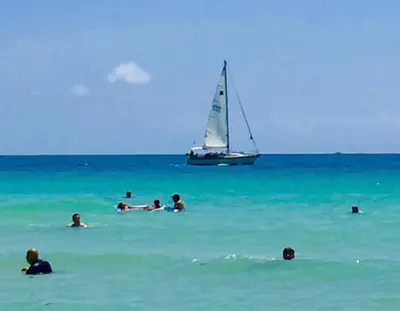 a group of people swimming in the ocean with a sail boat at Ocean Front Resort Studio in Miami Beach