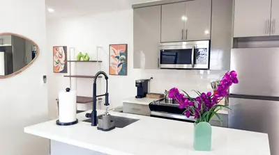 a kitchen with a vase of purple flowers on a counter at Cloud Nine - Wilton Drive Jacuzzi Backyard in Fort Lauderdale