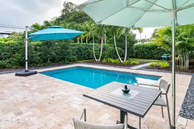 a table with an umbrella next to a swimming pool at Stylish 2BR Oasis with Pool Mini Golf & BBQ in Fort Lauderdale