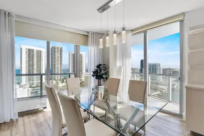 a dining room with a glass table and chairs and large windows at Luxury Oceanview Condo with Private Foyer at Beachwalk Resort in Hallandale Beach