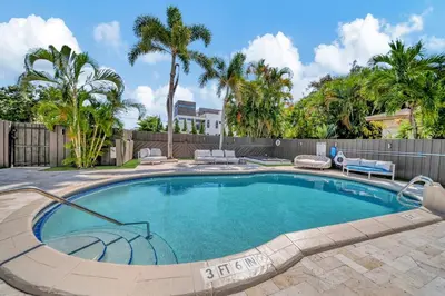 a swimming pool in a yard with a fence and palm trees at Waterfront Unit #1 20 Min Walk to Beach and Shops in Fort Lauderdale