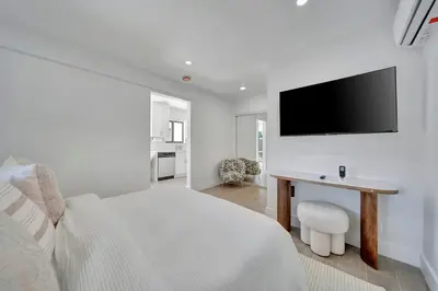 a white bedroom with a bed and a desk with a television at Waterfront Unit #1 20 Min Walk to Beach and Shops in Fort Lauderdale