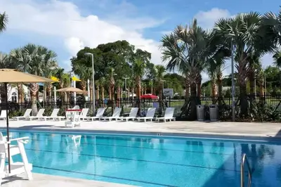 a pool with chairs and umbrellas and palm trees at Classy 2BR-2BA Oasis Beach Pool Parking EV Station in Hallandale Beach