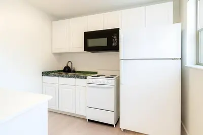 a white kitchen with a refrigerator and a microwave at Modern 2BR Stay with Desk, Patio, BBQ, Free Parking in Fort Lauderdale