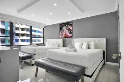 a bedroom with two beds and a chair and windows at Beachfront Luxury Alexander Unit, Pool Gym Parking in Miami Beach