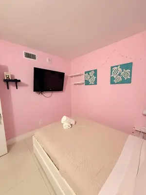 a pink bedroom with a bed and a flat screen tv at Modern 2BR beachfront with pool & tennis view in Sunny Isles Beach