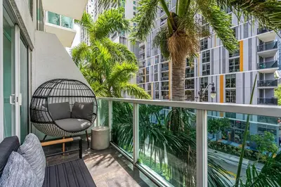 a balcony with a rattan chair and palm trees at Urban Oasis 2BR Loft Residence in Brickell in Miami