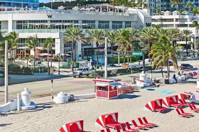 a beach with lounge chairs and palm trees and a building at The W 1906 in Fort Lauderdale