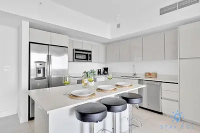a white kitchen with white cabinets and bar stools at Beachwalk Condo in Hallandale Beach