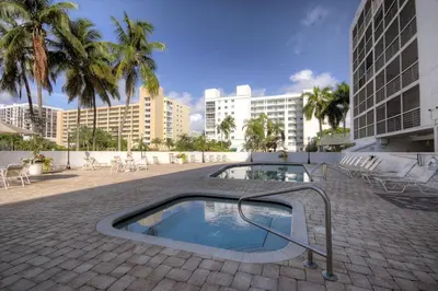 a swimming pool with chairs and palm trees and buildings at Le Frontenac 210 STR-01055 in Sunny Isles Beach