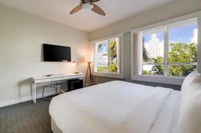 a bedroom with a bed and a desk and windows at Crest Hotel Suites in Miami Beach