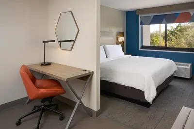 a bedroom with a bed and a desk and a bed and a chair at Holiday Inn Express Hotel & Suites Kendall East-Miami by IHG in Kendall