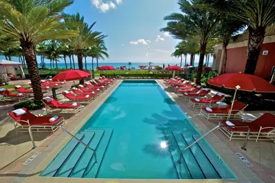 a swimming pool with chairs and red umbrellas at Acqualina Resort and Residences in Miami Beach