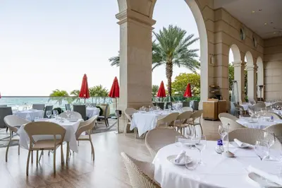 a restaurant with white tables and chairs and the ocean at Acqualina Resort and Residences in Miami Beach