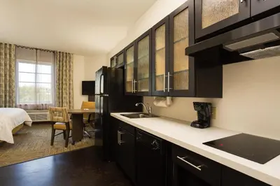 a kitchen with black cabinets and a sink and a bedroom at Candlewood Suites Fort Lauderdale Airport-Cruise by IHG in Fort Lauderdale