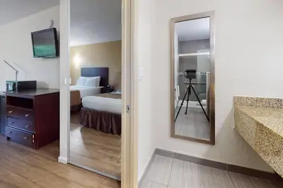 a bathroom with a bedroom with a bed and a mirror at Rodeway Inn & Suites Fort Lauderdale Airport & Cruise Port in Fort Lauderdale