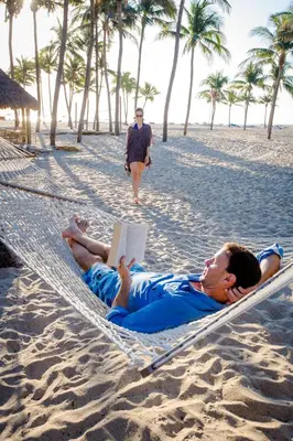 two men laying in a hammock on the beach with a book at The Lago Mar Beach Resort and Club in Fort Lauderdale