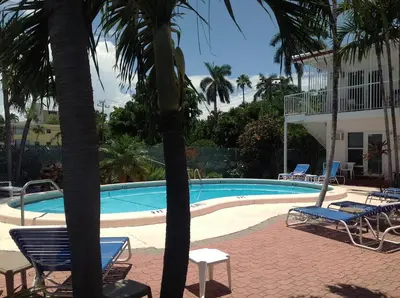 a swimming pool with chairs and palm trees next to a house at Birch Patio Motel in Fort Lauderdale