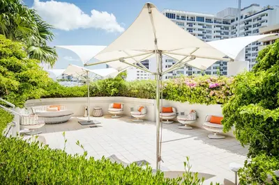 a patio with a white umbrella and chairs and bushes at Iberostar Waves Berkeley Shore in Miami Beach