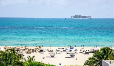a beach with chairs and a cruise ship in the ocean at The Sagamore Hotel South Beach in Miami Beach