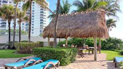 a straw hut with chairs and tables and palm trees at The Tides-1 bedroom apartment Ground Floor in Hollywood