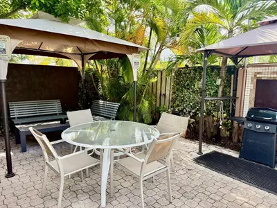 a glass table and chairs on a patio with a grill at Sheridan Guesthouse in Dania Beach