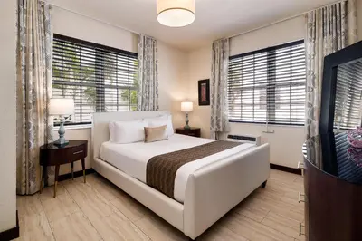 a bedroom with a bed and a tv and windows at Tradewinds Apartment Hotel Miami Beach in Miami Beach