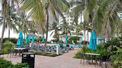 a pool with tables and chairs and palm trees at 2 BEDROOMS 2 FULL BATHROOMS APT. ON THE BEACH in Hollywood