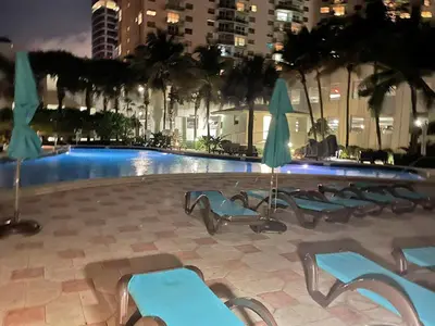 a swimming pool with blue chairs and umbrellas at night at 2 BEDROOMS 2 FULL BATHROOMS APT. ON THE BEACH in Hollywood