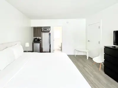 a white bedroom with a large bed and a kitchen at Beach Gardens in Fort Lauderdale