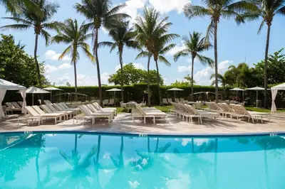 a pool with chairs and umbrellas and palm trees at Hilton Bentley Miami South Beach in Miami Beach