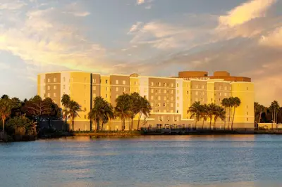 a large building with palm trees in front of the water at Homewood Suites Miami Airport/Blue Lagoon in Miami