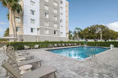 a swimming pool with chairs and a building at Homewood Suites Miami Airport/Blue Lagoon in Miami
