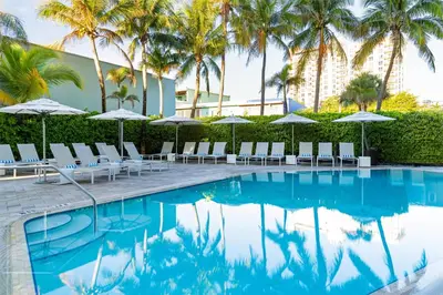 a pool with chairs and umbrellas and palm trees at Sonesta Fort Lauderdale Beach in Fort Lauderdale