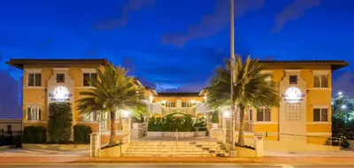 a yellow building with palm trees in front of it at Sun Harbour Boutique Hotel in Miami Beach