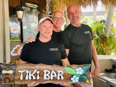 three men posing for a picture with a tiki bar sign at The Cabanas Guesthouse & Spa - Gay Resort catering to Gay Men in Fort Lauderdale