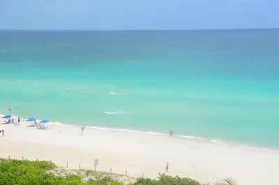 a beach with people walking on the sand and the ocean at New Point Miami Beach Apartments in Miami Beach