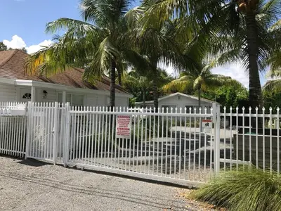 a white fence in front of a house with palm trees at Grove Bay Bungalow - 2/2 Gated Cottage-Walk to Bay in Miami