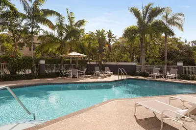 a swimming pool with chairs and umbrellas and palm trees at Hampton Inn Pembroke Pines in Pembroke Pines