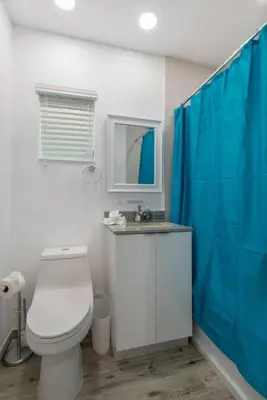 a bathroom with a toilet and a blue shower curtain at Renovated studio w ocean views boardwalk steps in Hollywood
