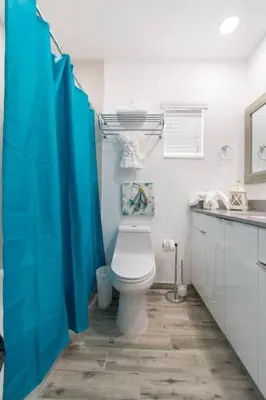 a bathroom with a toilet and a blue shower curtain at Modern apartment wbeach steps parking in Hollywood