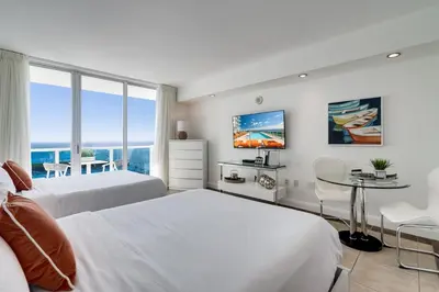 a bedroom with two beds and a table and a tv at Ocean View Balcony steps from Restaurants, Peacock Park & Marina in Miami