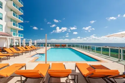a swimming pool with orange lounge chairs and the ocean at City View Balcony steps from Restaurants, Peacock Park & Marina in Miami