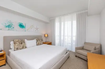 a white bedroom with a bed and a chair at Private Ocean Luxury Condos at Beachwalk Resort in Hallandale Beach