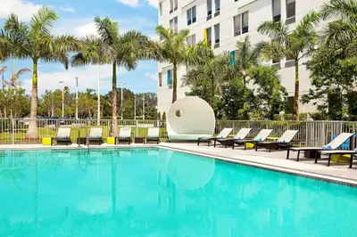 a swimming pool with chairs and palm trees in front of a building at Aloft Miami Doral in Miami