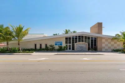a building with palm trees in front of a street at Downtown Hollywood Gardens Inn & Suites in Hollywood